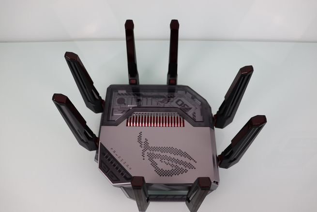 Vista superior de un router ASUS ROG Rapture GT-BN98 con ocho antenas externas y logotipo iluminado sobre una superficie blanca.