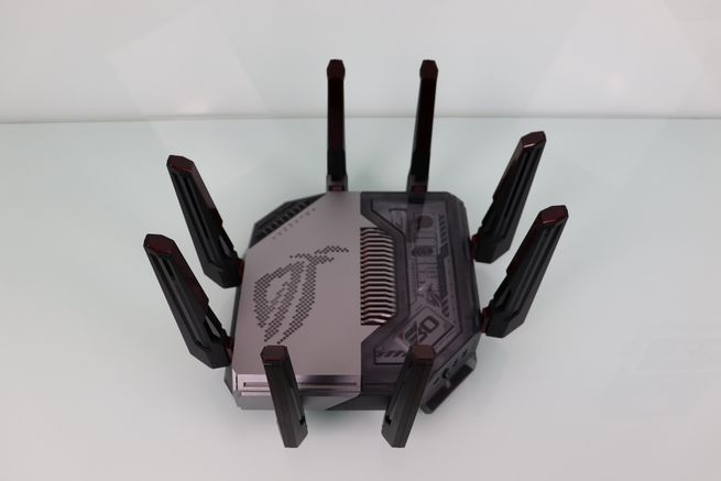 Plano general del router ASUS GT-BN98 con sus ocho antenas desplegadas en forma de araña sobre una superficie clara.