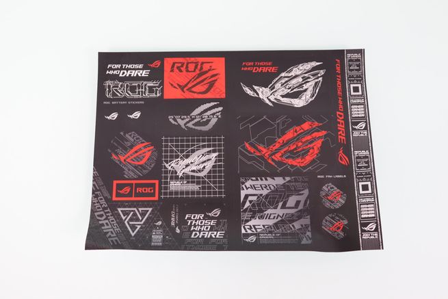 Pliego de pegatinas decorativas de la línea ASUS ROG con logotipos en rojo, blanco y gris sobre fondo negro.