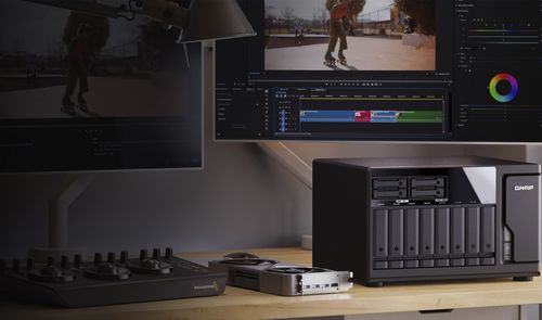 Servidor NAS QNAP TVS-h1277AX en un escritorio junto a monitores con software de edición de vídeo.