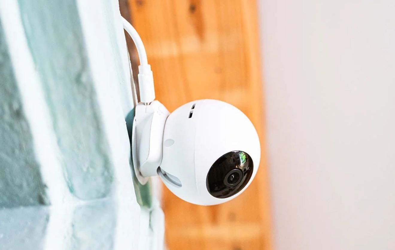 Cámara de vigilancia Shelly de forma esférica instalada en una pared interior blanca al lado de una viga de madera.