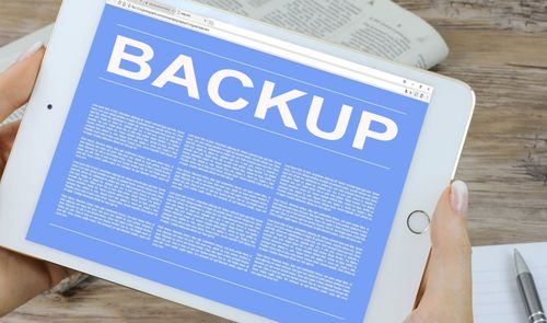 Tableta blanca que muestra en pantalla la palabra BACKUP sobre un fondo azul con texto descriptivo.