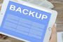 Tableta blanca que muestra en pantalla la palabra BACKUP sobre un fondo azul con texto descriptivo.