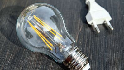 Bombilla eléctrica de filamento LED apagada junto a un enchufe blanco sobre fondo oscuro.