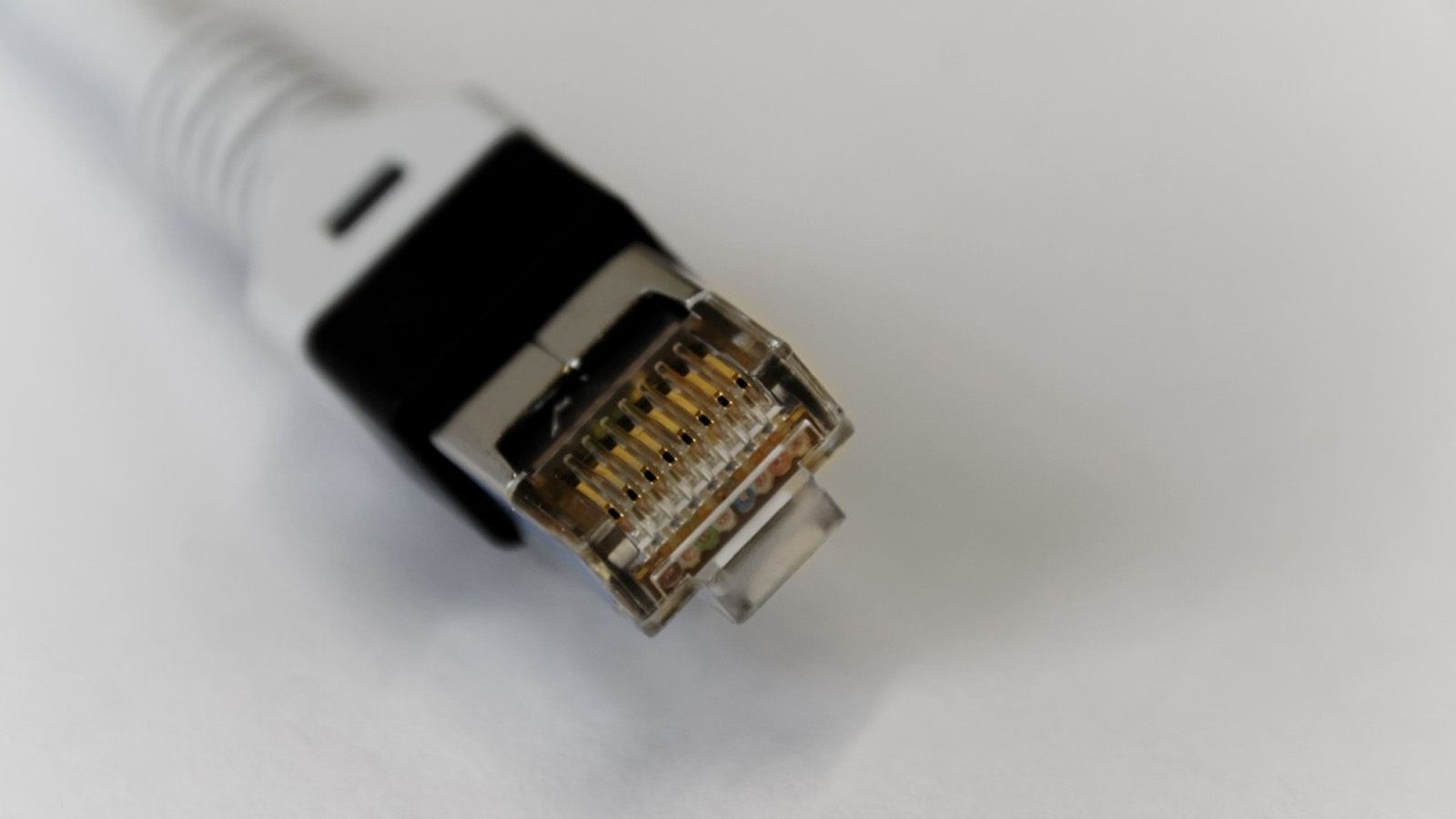 Primer plano de un conector RJ45 de un cable Ethernet con blindaje metálico y contactos dorados.
