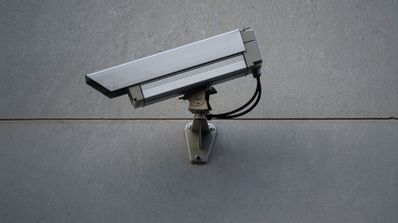 Cámara de vigilancia exterior de carcasa metálica instalada en una fachada gris.