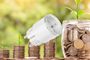 Enchufe inteligente sobre pilas de monedas y plantas que simbolizan el ahorro energético