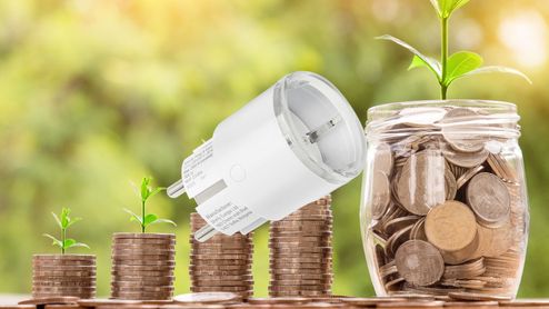 Enchufe inteligente sobre pilas de monedas y plantas que simbolizan el ahorro energético