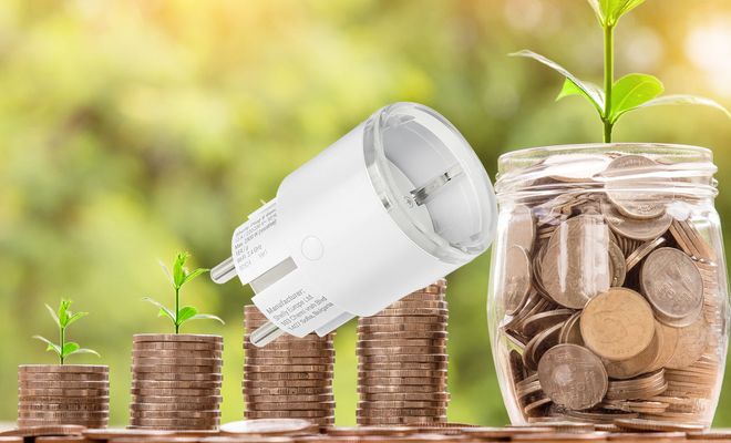 Enchufe inteligente sobre pilas de monedas y plantas que simbolizan el ahorro energético
