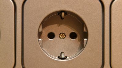 Primer plano de una toma de corriente de pared tipo Schuko instalada en un panel metálico.