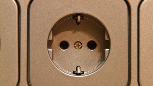Primer plano de una toma de corriente de pared tipo Schuko instalada en un panel metálico.