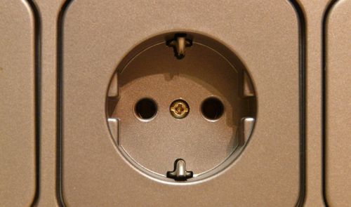 Primer plano de una toma de corriente de pared tipo Schuko instalada en un panel metálico.