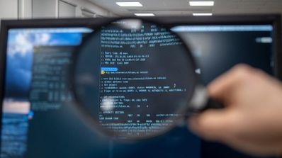 Una lupa amplía líneas de código informático en la pantalla de un monitor para detectar errores.