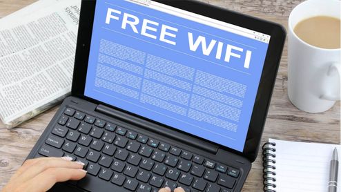 Pantalla de una tablet con teclado mostrando un aviso publicitario de Free Wi-Fi sobre una mesa con café y periódico.