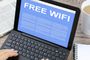 Pantalla de una tablet con teclado mostrando un aviso publicitario de Free Wi-Fi sobre una mesa con café y periódico.