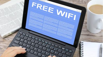 Pantalla de una tablet con teclado mostrando un aviso publicitario de Free Wi-Fi sobre una mesa con café y periódico.
