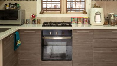 Cocina moderna con encimera blanca, fogones de gas, horno integrado y mobiliario de madera laminada.