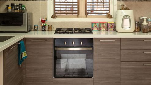 Cocina moderna con encimera blanca, fogones de gas, horno integrado y mobiliario de madera laminada.