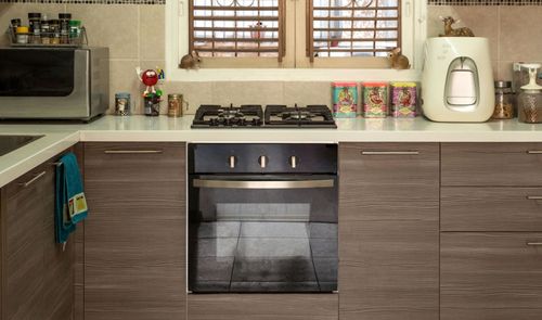 Cocina moderna con encimera blanca, fogones de gas, horno integrado y mobiliario de madera laminada.