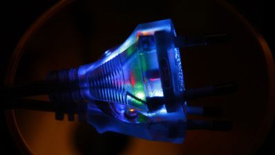 Primer plano de un enchufe eléctrico transparente con luces LED de colores en su interior iluminado en la oscuridad.