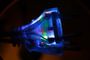 Primer plano de un enchufe eléctrico transparente con luces LED de colores en su interior iluminado en la oscuridad.