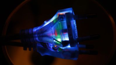 Primer plano de un enchufe eléctrico transparente con luces LED de colores en su interior iluminado en la oscuridad.
