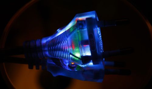 Primer plano de un enchufe eléctrico transparente con luces LED de colores en su interior iluminado en la oscuridad.