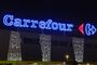 Rótulo luminoso azul de Carrefour en la fachada de un hipermercado por la noche.