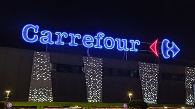 Rótulo luminoso azul de Carrefour en la fachada de un hipermercado por la noche.