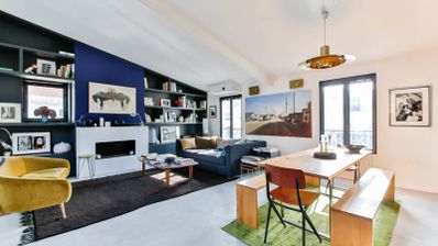 Salón comedor moderno con estantería integrada en la pared, chimenea, sofá azul y mesa de madera con bancos.