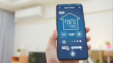 Mano sujetando un teléfono móvil con una aplicación de Smart Home abierta para controlar la temperatura del hogar.