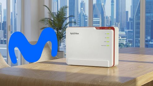 Router FRITZ!Box sobre una mesa de madera junto al logotipo de Movistar con vistas a una ciudad de fondo.