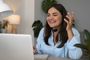 Mujer sonriente con auriculares y micrófono hablando frente a su ordenador portátil durante una videollamada.