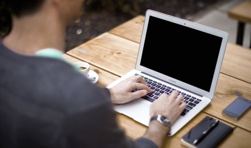 Primer plano de las manos de una persona escribiendo en el teclado de un ordenador portátil sobre una mesa de madera.