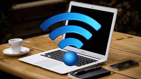 Ordenador portátil abierto sobre una mesa de madera con un gran símbolo tridimensional de Wi-Fi azul delante de la pantalla.