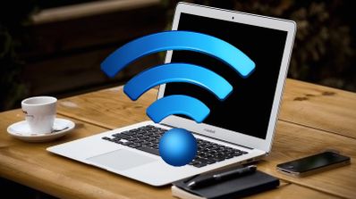 Ordenador portátil abierto sobre una mesa de madera con un gran símbolo tridimensional de Wi-Fi azul delante de la pantalla.