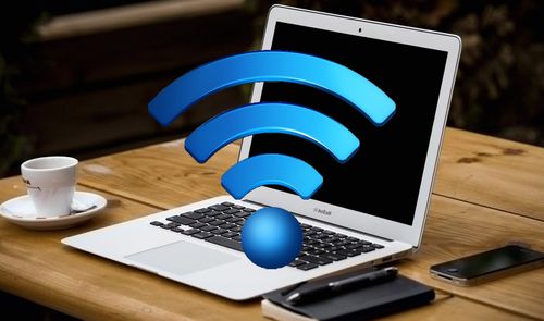 Ordenador portátil abierto sobre una mesa de madera con un gran símbolo tridimensional de Wi-Fi azul delante de la pantalla.