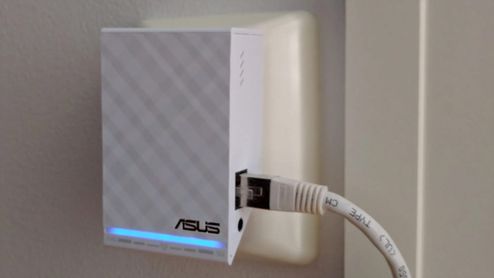 Repetidor Wi-Fi ASUS blanco con cable Ethernet conectado y luz LED azul encendida.