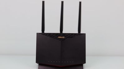 Router inalámbrico ASUS RT-AX86U de color negro con tres antenas externas sobre una superficie blanca.