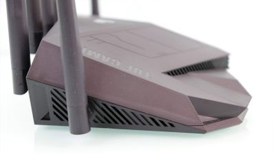 Vista de perfil del router gaming ASUS TUF Gaming TUF-AX5400 donde se aprecian las rejillas de ventilación laterales y su diseño angular sobre fondo blanco.