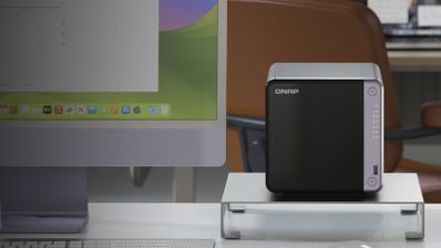 Servidor NAS de la marca QNAP situado en un escritorio junto a un ordenador monitor de gran formato.