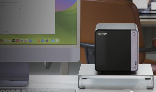 Servidor NAS de la marca QNAP situado en un escritorio junto a un ordenador monitor de gran formato.