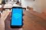 Mano sosteniendo un teléfono móvil que muestra el icono de conexión Wi-Fi en pantalla sobre un fondo de mesas de madera.
