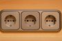 Tres tomas de corriente Schuko integradas en un marco triple de color gris sobre una superficie de madera.