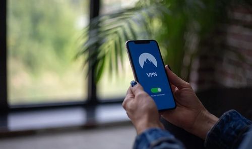 Persona sujetando un teléfono móvil con una aplicación de VPN activada en la pantalla.