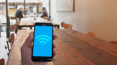 Mano sosteniendo un teléfono móvil con el icono de señal Wi-Fi en pantalla en el interior de una cafetería.