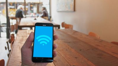 Mano sosteniendo un teléfono móvil con el icono de señal Wi-Fi en pantalla en el interior de una cafetería.