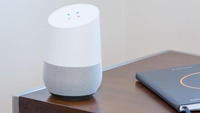 Altavoz inteligente de cuerpo blanco y base gris sobre una mesa de madera.