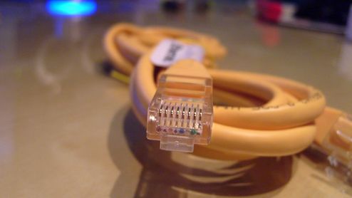 Primer plano de un conector RJ45 de un cable Ethernet amarillo enrollado sobre una mesa.