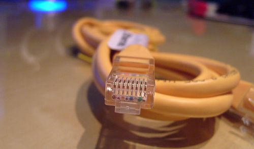Primer plano de un conector RJ45 de un cable Ethernet amarillo enrollado sobre una mesa.